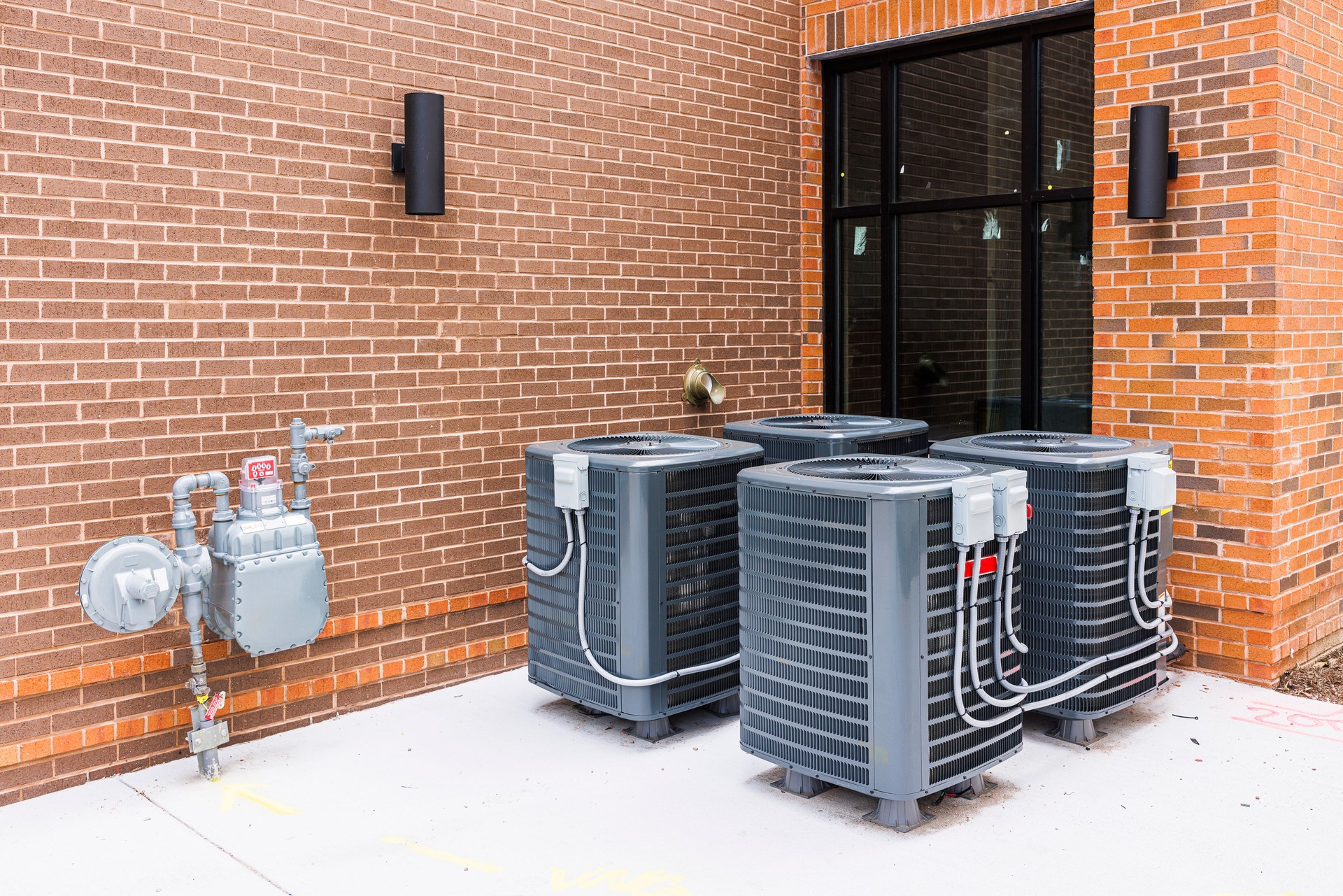 Air conditioning sets and gas meter near a brick wall. Mini air cooling chillers and heat pumps near the window